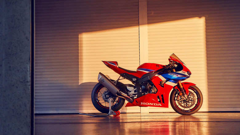 A red, white, and blue 2025 Honda CBR1000RR-R SP Fireblade motorbike parked against a sun-kissed industrial building.