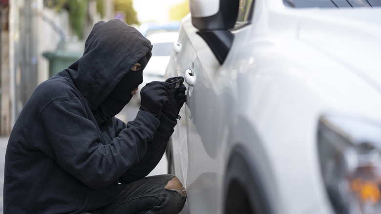 A masked person stealing a white car