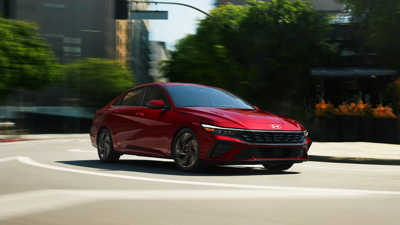 2025 Hyundai Elantra in red driving through a city street, showcasing its sharp front-end design and dynamic lines with blurred urban surroundings.