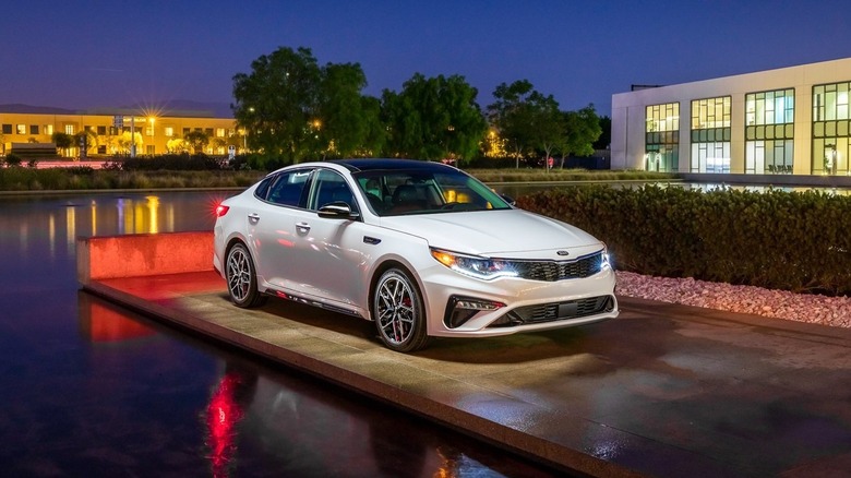 A white Kia Optima for the 2020 Model year on a platform next to a water feature