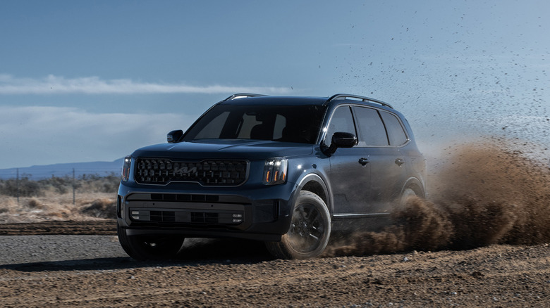 A navy blue 2025 Kia Telluride that's on gravel and throwing up dirt behind it