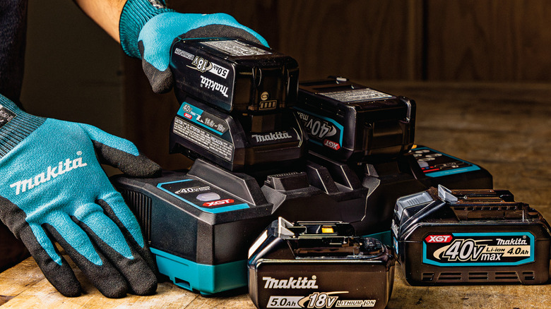 person with gloves holding Makita batteries