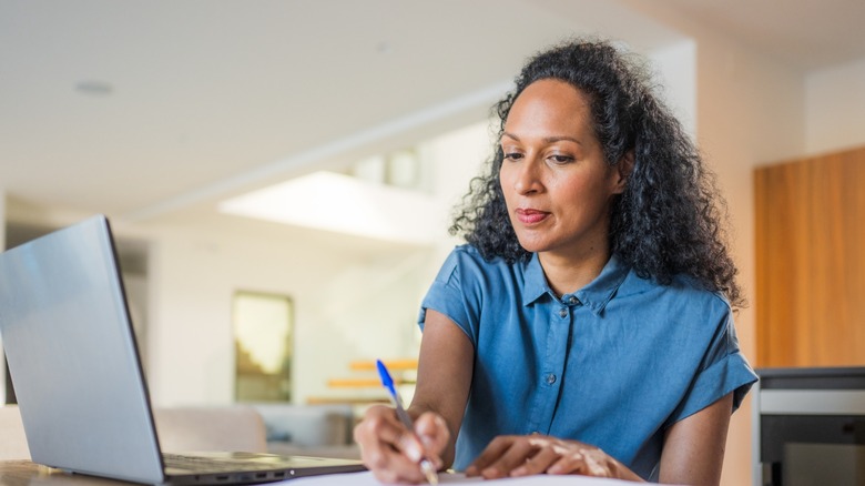A Woman Studying Information On A PC And Taking Notes
