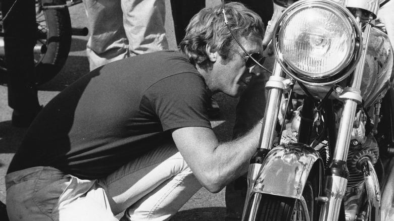 Steve McQueen tinkering with motorcycle