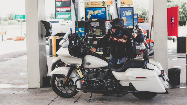 A person filling up their Harley-Davidson motorcycle at a gas station.