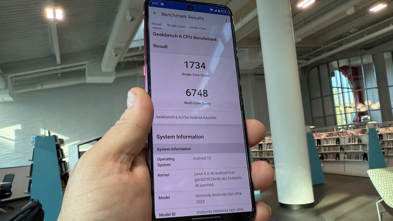 A man holds the Moto Razr Ultra in his hand with Geekbench scores on the scree