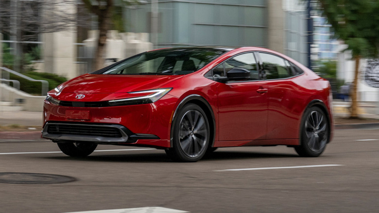 Supersonic Red Toyota Prius XLE driving down a road, trees and buildings in the background, front 3/4 view