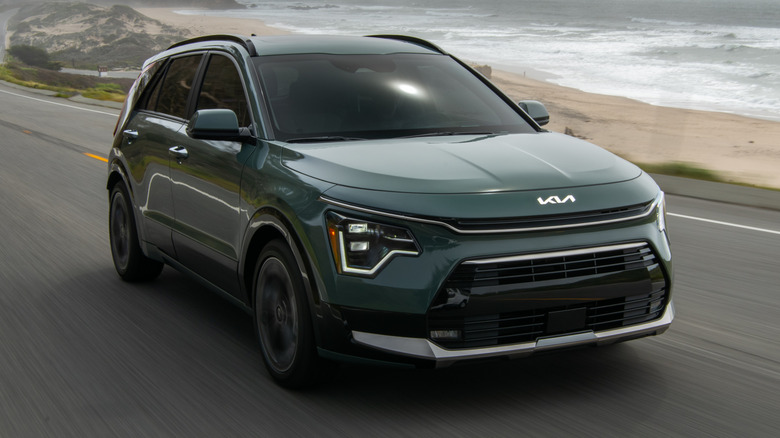 2024 Kia Niro driving on a road next to a sandy beach and the ocean