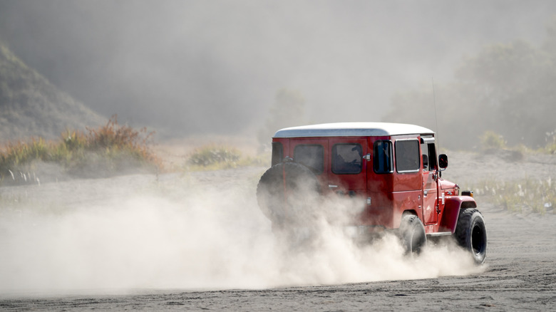 A red FJ40 Toyota Land Cruiser kicking up some dust, rear 3/4 view
