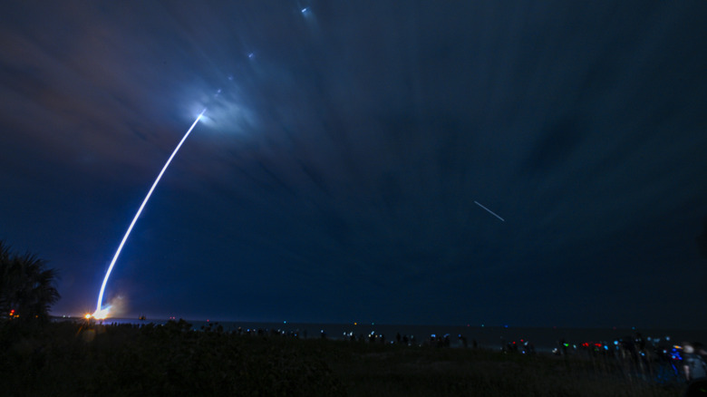 The trail of a rocket launching up into the night sky.