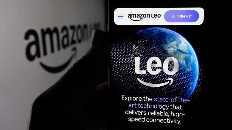 A shadowed hand holding a phone with the Amazon Leo logo.