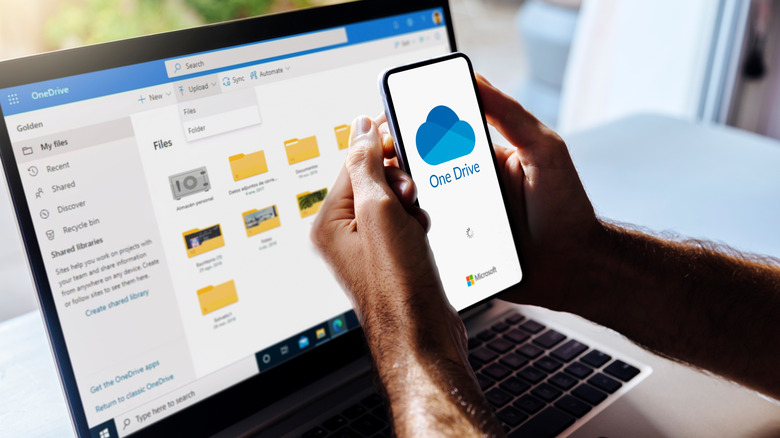 OneDrive on mobile phone and computer. Man holding a mobile phone with Microsoft cloud storage app on the screen.