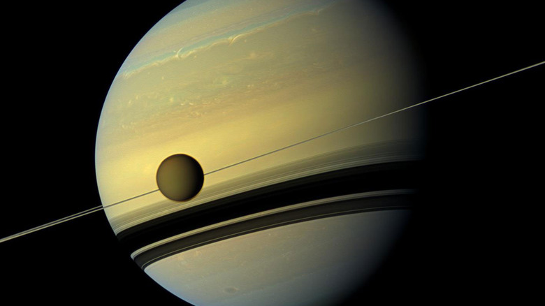 Saturn's largest moon Titan shown in front of Saturn with rings flat against the horizon