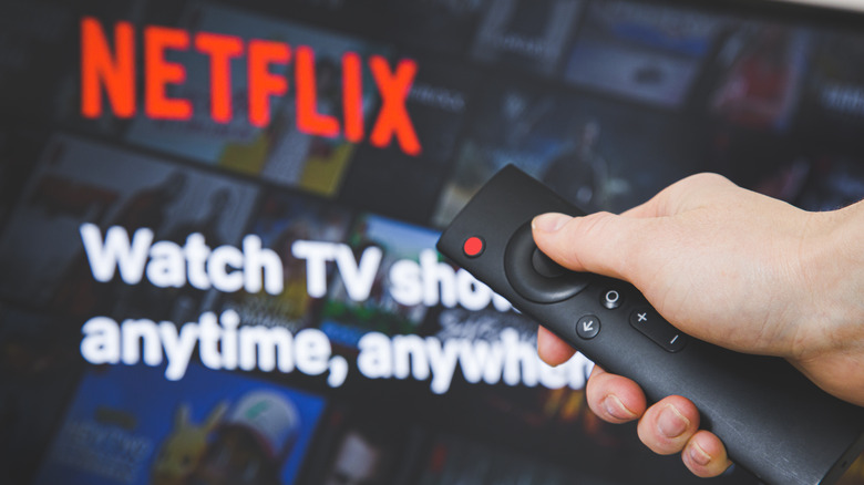 Hand holding a remote in front of a TV displaying Netflix