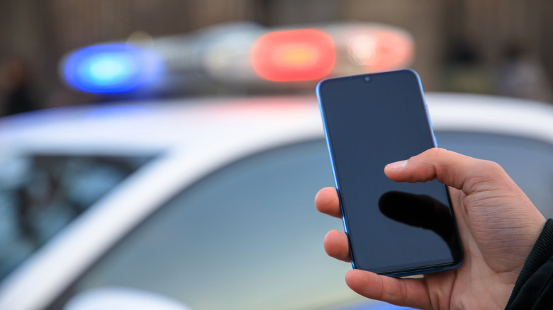 Person holding smartphone with police car blurred in background