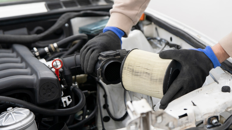 A mechanic changing the air filter in the engine bay of a vehicle with the hood open.