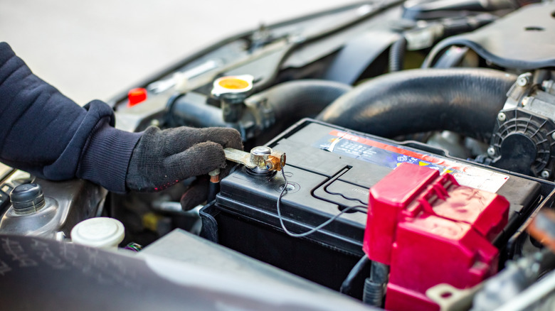 A man wearing gloves loosening a car battery terminal connections using a torque wrench.