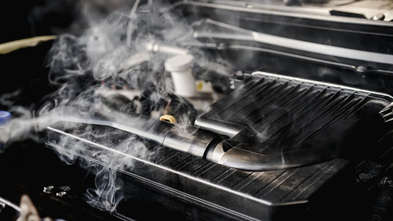 The engine of an unknown model vehicle overheating with steam coming out of some areas.