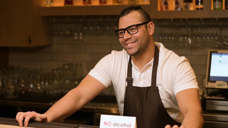 A bartender posing with a "No Alcohol" sign.