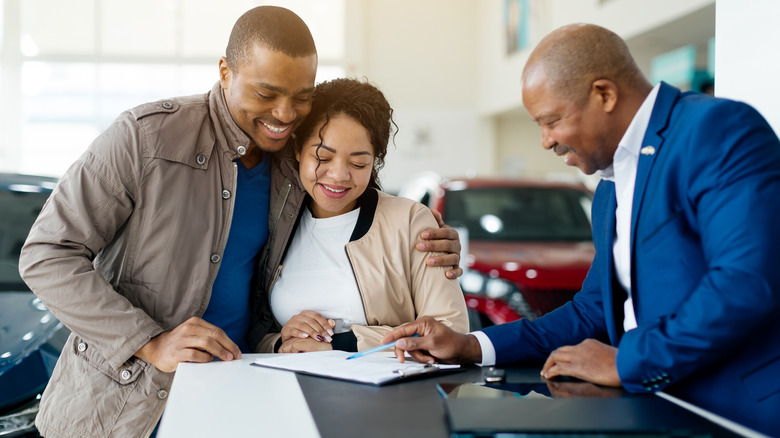 A couple signing a lease at a dealership lot.