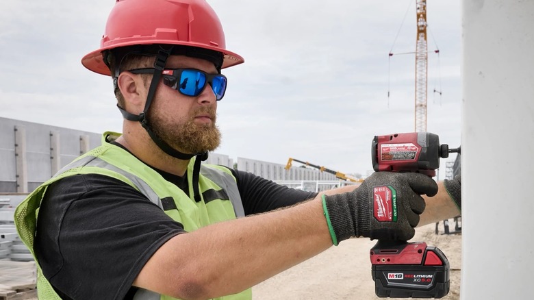 Man wearing a hardhat and Milwaukee safety glasses drills into a wall