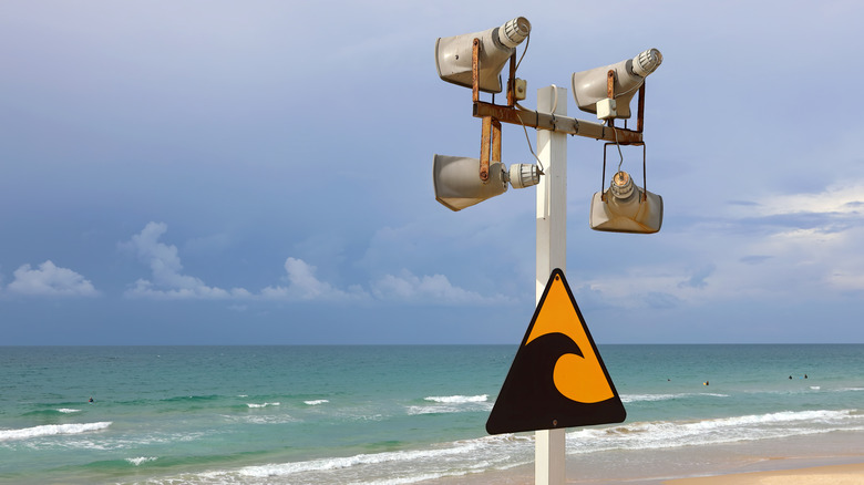 A sign warning of tsunamis on a post with speakers and a beach in the background