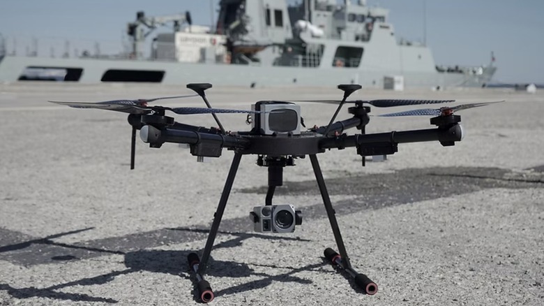 An ORKA quadcopter sitting on asphalt beside a military ship