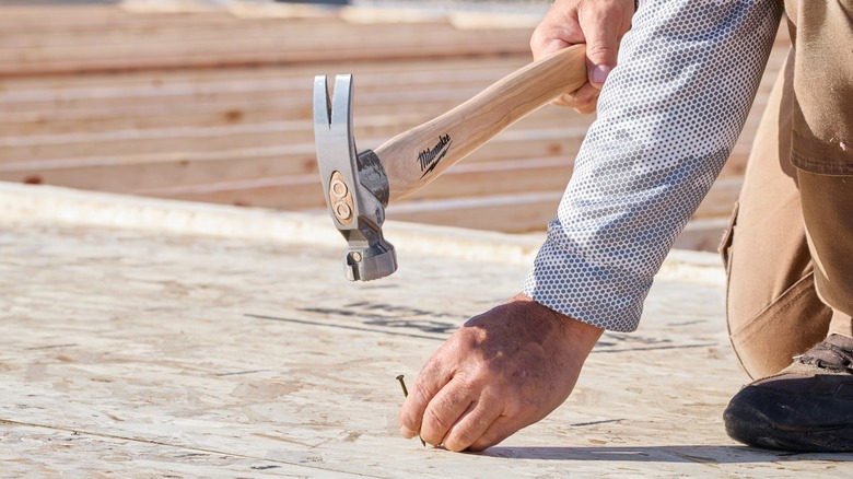 A person using a Milwaukee hammer on wood.