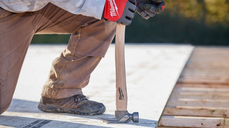 A person removing a nail with a Milwaukee hammer.