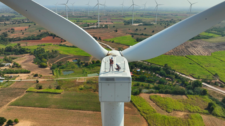 Wind turbine with two construction workers on top, overlooking wind farm