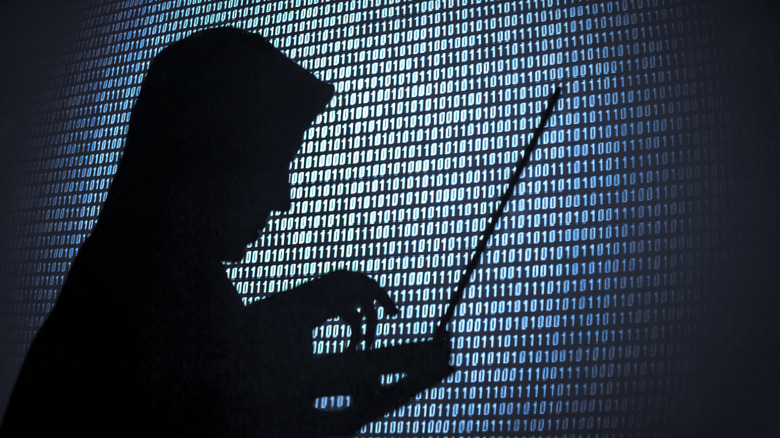man with hood on looking at codes on laptop