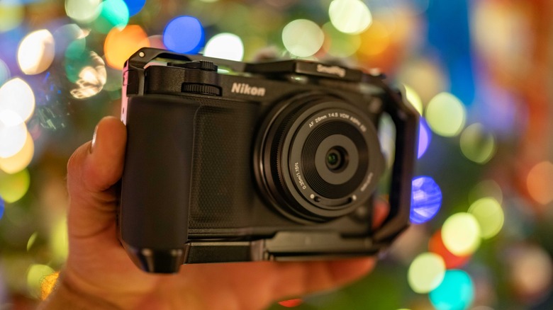 The Nikon Zr with the Viltrox AF 28mm f/4.5 lens held in a hand in front of blurry holiday lights.