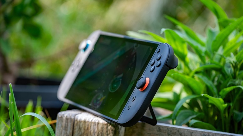 The Nintendo Switch 2 on the edge of a planter in a garden.