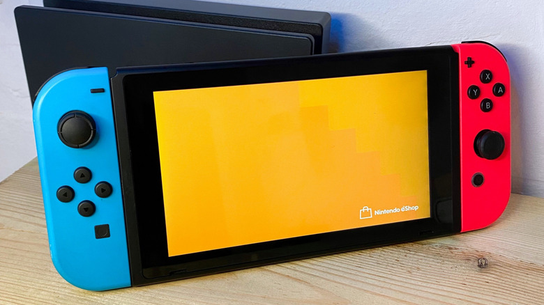 A Nintendo Switch with blue and red joycons in handheld mode showing an orange screen for the Nintendo eShop.