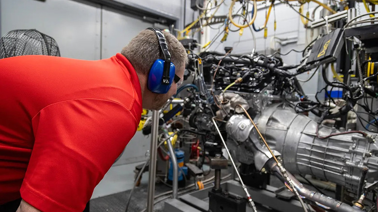 Nissan engineer inspecting VQ38DD engine on dynamometer stand.