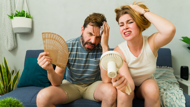 Stressed couple trying to cool off during summer heat wave at home