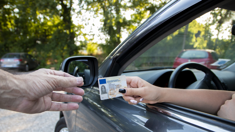 Driver handing driver's license to person through window