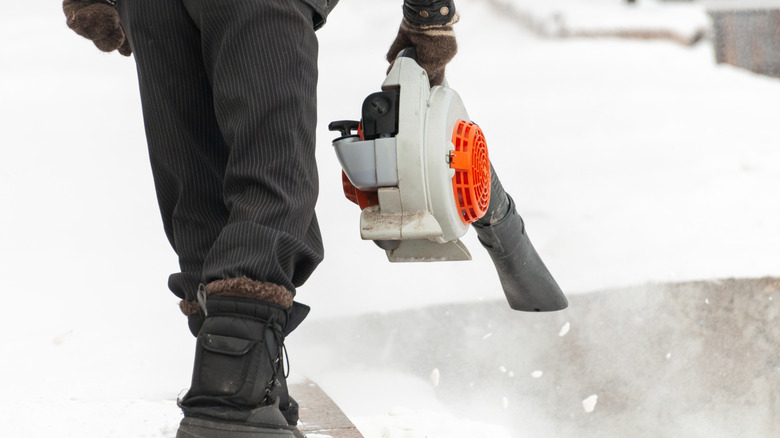 A man in boots cleaning snow off the pavement with a leaf blower