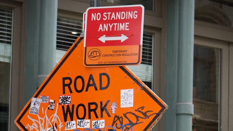 'No Standing Anytime' sign with double-headed arrow clipped on a large orange 'Road Work Ahead' construction sign