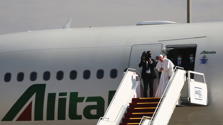 Pope Francis bows before boarding an airplane.