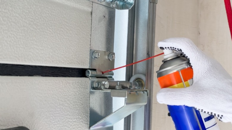 Gloved hands holding a can of lubricant at a garage door
