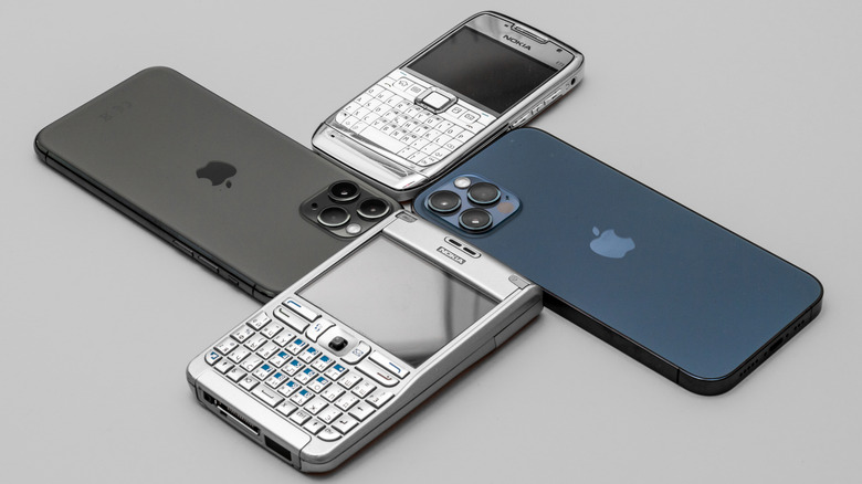 Vintage Nokie phones sitting next to black and blue Apple iPhones