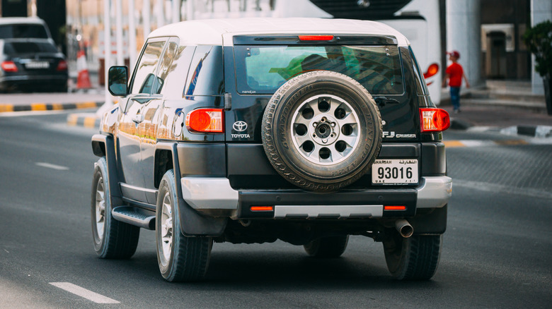 A Toyota FJ Cruiser with an exposed rear-mounted spare tire running on the road.