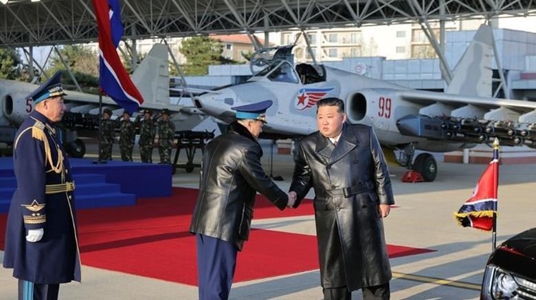 DPRK leader Kim Jong Un shaking a man's hand before several Su-25 fighter jets