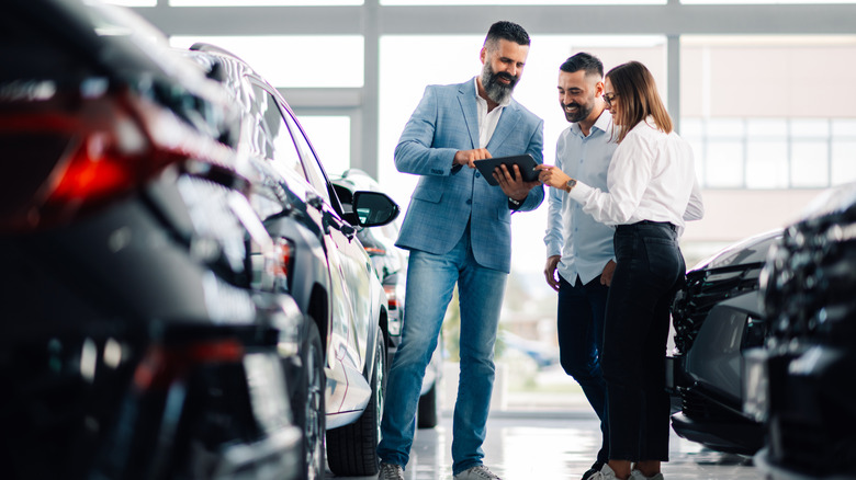 man selling car to a couple at a car dealership
