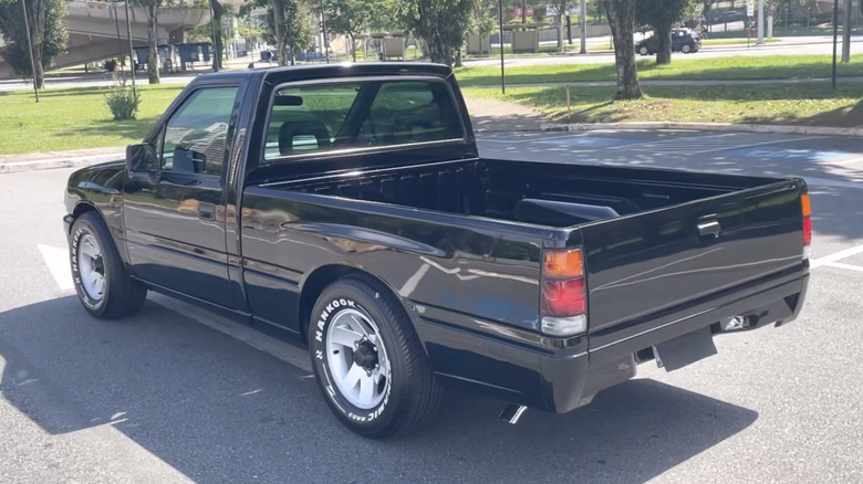 Rear three-quarter view of a black 1990s Isuzu pickup truck in a parking lot.