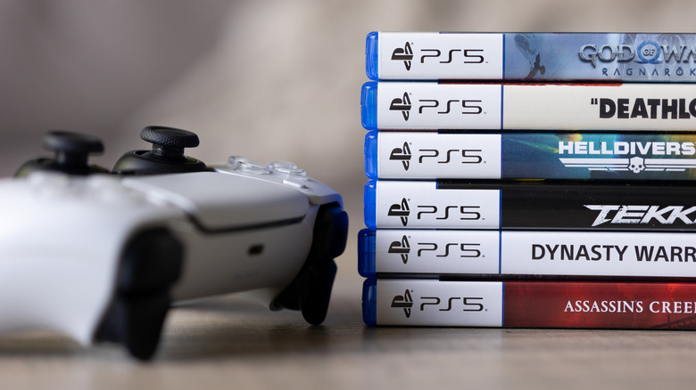 A stack of PlayStation 5 games with a DualSense controller.
