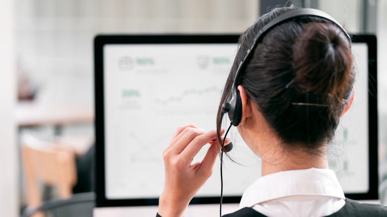 shot of a woman from behind at a desk in front of a computer wearing a headset with a microphone for customer service