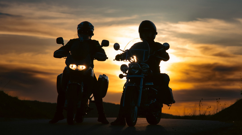 Silhouette of motorcyclists riding at sunset, with one motorcycle using headlights.