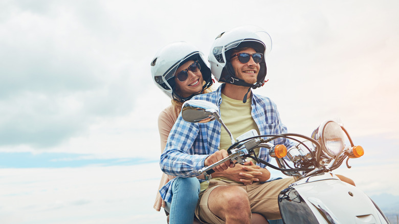 Couple on motor scooter wearing white motorcycle helmets.